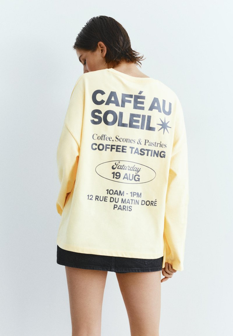 Personne aux cheveux courts et foncés portant une chemise jaune pâle à manches longues avec un texte noir annonçant un événement de dégustation de café à Paris le 19 août.