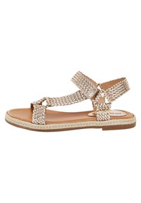 Vävd metallisk beige sandal med platt sula, en ankelrem och dubbla framband. Har en texturerad yta och flätad kantdetalj.
