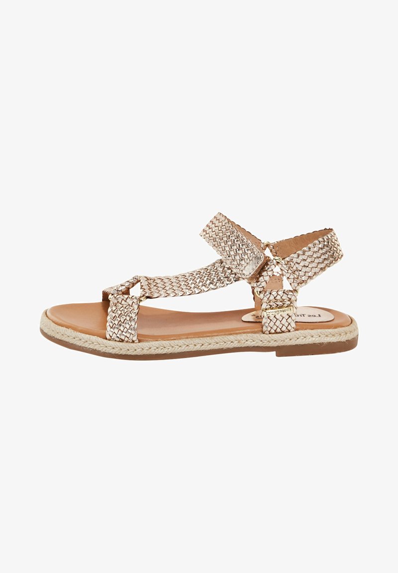 Vävd metallisk beige sandal med platt sula, en ankelrem och dubbla framband. Har en texturerad yta och flätad kantdetalj.