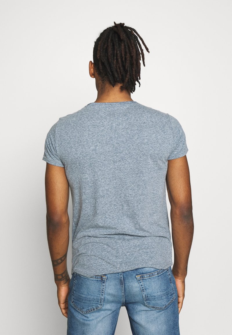 Grå kortärmad t-shirt i mjukt tyg, med rund halsringning och en avslappnad passform, kombinerad med blå jeans.