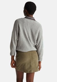 Šedý pletený svetr s krátkým střihem a žebrovanými manžetami, doplněný khaki manšestrovou sukní se zipem na boku.