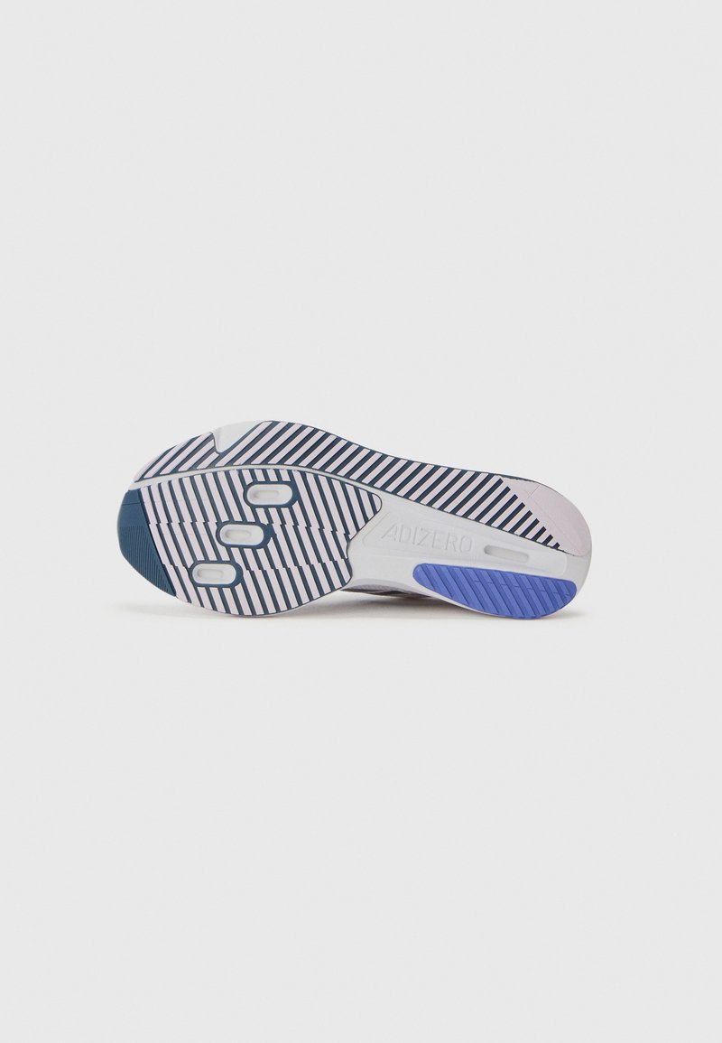 La suela de la zapatilla deportiva presenta una base blanca con acentos en marino y morado, rayas texturizadas y tres almohadillas circulares para mayor agarre.