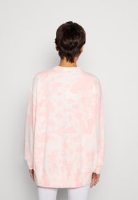 Sudadera de gran tamaño en blanco con un patrón de tie-dye en rosa. Presenta mangas largas, puños de canalé y un escote redondeado. Textura suave.