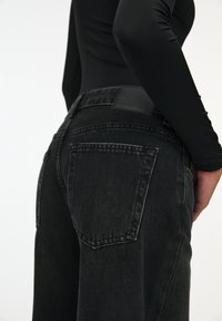 Jean en denim noir à coupe ample, avec des poches arrière et un patch en cuir portant l'inscription "PULL&BEAR" à la taille. Texture douce et finition délavée.