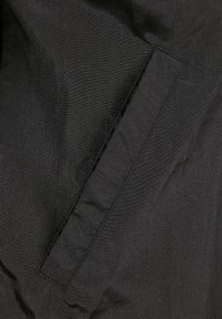 Juodas audinio švarkas su lygiu, šiek tiek blizgiu paviršiumi. Yra siuvinėtas šoninis kišenė ir santūrus dizainas.