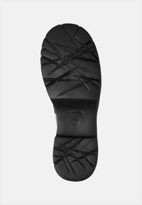 Semelle de chaussure noire avec des rainures profondes entrecroisées et un numéro de pointure 38 marqué près du talon sur un fond blanc.