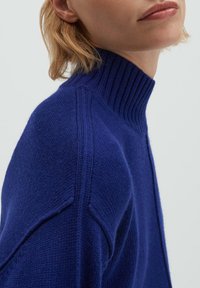 Pull en maille bleu roi avec un col montant côtelé, une coupe légèrement ample et des épaules tombantes, présentant une finition texturée.