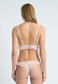 Conjunto de lencería rosa que incluye un bralette con volantes y tirantes finos, y un tanga a juego, fabricado en material translúcido con bordado floral y bordes festoneados.