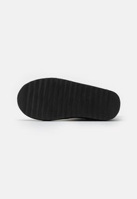 Suela de zapato de goma negra con una superficie texturizada y estriada para mayor tracción, de forma ovalada y con un tacón ligeramente elevado.