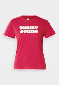 Fuksiatoonist puuvillane t-särk, mis on varustatud ümmarguse kaelus ning lühikeste varrukatega. Esiosas on suured valged nõgese kirjutisega "TOMMY JEANS".