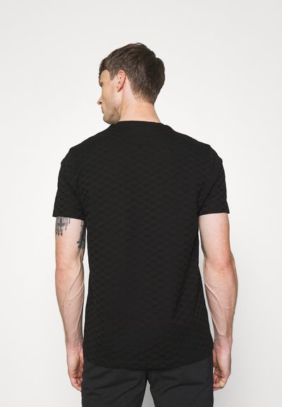 Camiseta negra de manga corta con un patrón texturizado, escote redondo y un corte relajado. La tela parece suave con un sutil detalle.