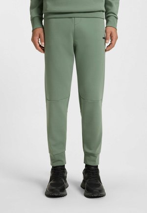 Green fleece joggers with a slim fit; features paneling at knees, ribbed cuffs, and a subtle logo on the hip. Worn with black sneakers.