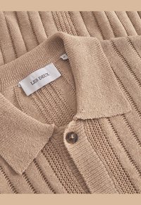 Beżowy sweter polo z dzianiny o prążkowanej fakturze, z zapięciem na guziki oraz metką z napisem "LES DEUX" i etykietą rozmiaru.