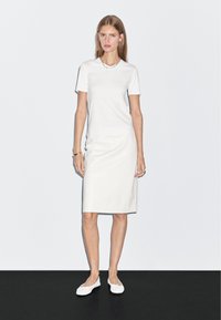 Biała sukienka t-shirtowa o prostym kroju i krótkich rękawach. Gładka tekstura, zestawiona z białymi butami wsuwanymi. Prosty design i minimalne detale.