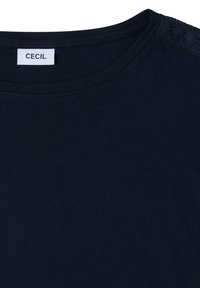 Chemise bleu marine foncé à col rond, avec une étiquette blanche indiquant "CECIL" à l'intérieur du col.