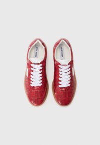 Chaussures de type sneaker rouges en matériau synthétique brillant avec un motif crocodile. Lacets blancs et une semelle en caoutchouc marron clair.