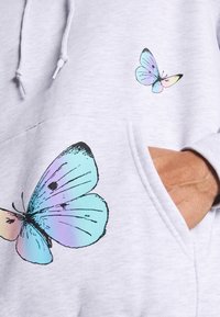 Grauer Kapuzenpullover mit großen, schwarz konturierten Schmetterlingsmotiven in Blau- und Pastelltönen, mit Fronttasche und Kapuze mit Kordelzug.