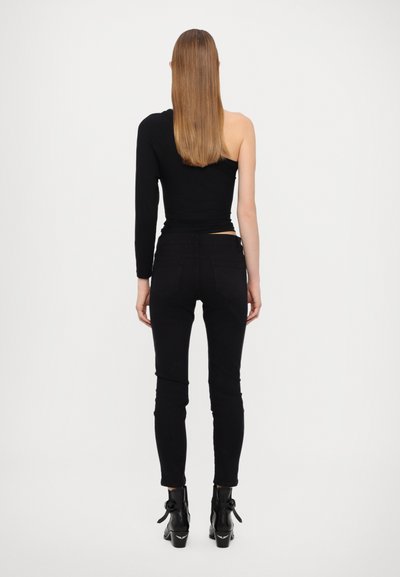 Svart én-skulder topp kombinert med svarte skinny jeans. Toppen har en tettsittende design, mens buksene har baklommer og ankel-lengde passform.