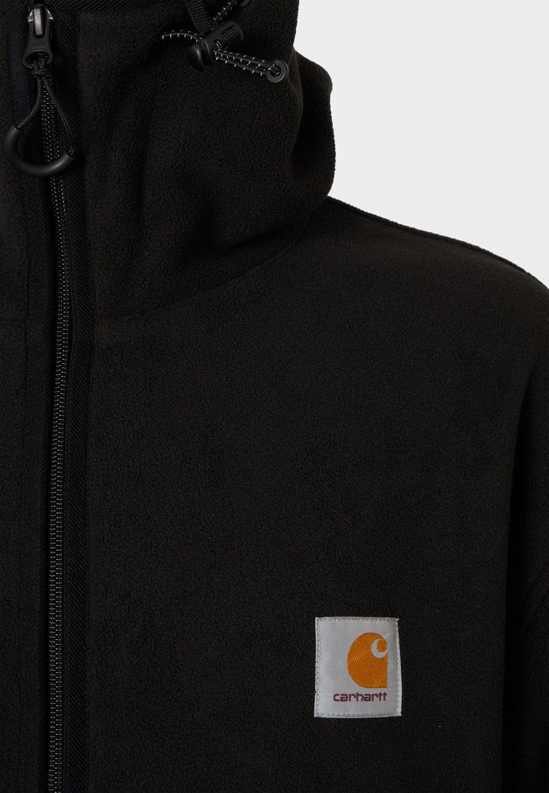 Haut de hoodies en polaire noire avec un col haut, fermeture éclair à l'avant et cordon de serrage. Présente une étiquette carrée avec un logo orange sur la poitrine gauche.