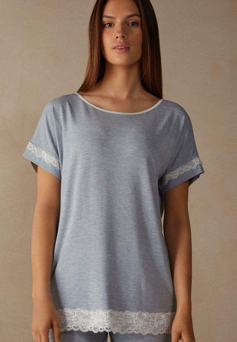 Grijze T-shirt met korte mouwen en ronde halslijn, voorzien van kantdetails op de mouwen en de zoom. Zachte textuur en een comfortabele pasvorm.