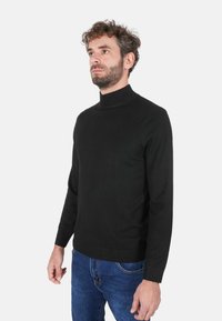 Maglione dolcevita nero dal design aderente. Realizzato in tessuto liscio con maniche lunghe, polsini a costine e orlo dritto.
