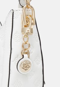 Vit läderhandväska med präglat blommönster, svart kant och guldfärgade detaljer. Har en dekorativ berlock och en robust remfäste.