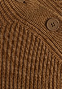 Tessuto a maglia marrone con texture a coste verticali. Presenta un grande bottone marrone in rilievo con la scritta "Marc O'Polo DENIM."