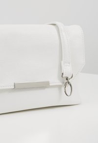 Sac à main en cuir blanc avec une fermeture métallique rectangulaire argentée et une petite dragonne amovible avec un crochet porte-clés argenté.