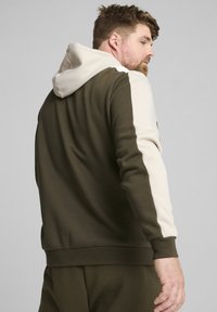 Sudadera con capucha que presenta un cuerpo verde oscuro, acentos color crema en la capucha y las mangas, y puños y dobladillo acanalados.