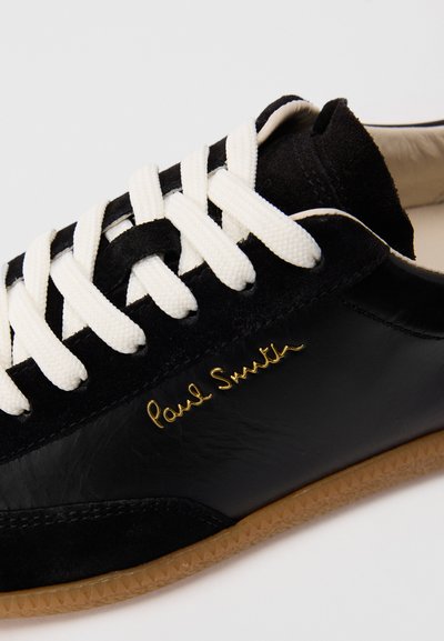 Sneaker nera in pelle e suede con lacci bianchi, suola in gomma e firma "Paul Smith" in oro sul lato.