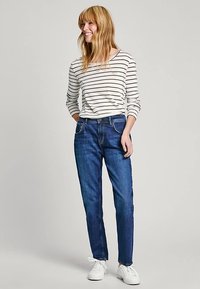 Siniset farkut suoralla istuvuudella, yhdistetty valkoiseen ja laivastonsiniraidalliseen pitkähihainen paitaan, viimeistelty valkoisilla tennareilla.