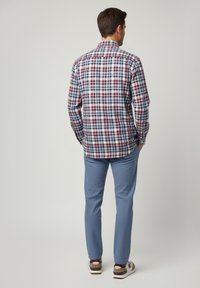 Camisa de botones a cuadros en rojo, azul marino y blanco. Combinada con pantalones azules texturizados y zapatillas casuales. Detalles visibles de costuras y cuello.