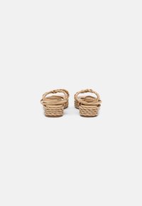 Tan braided slide sandals with a low, textured sole and delicate strap design. The material appears soft and pliable.
