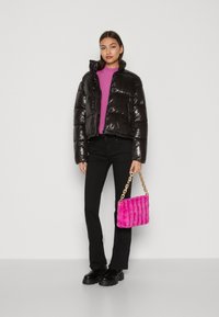 Chaqueta de plumas negra y brillante con un diseño corto, llevada sobre un suéter rosa brillante, combinada con pantalones negros y un bolso acolchado rosa.