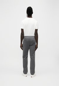 Pantaloni in velluto a coste grigio con vestibilità affusolata, caratterizzati da due tasche posteriori e una texture sottile, abbinati a una maglietta bianca a maniche corte semplice.