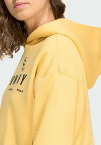 Felpa gialla con cappuccio e tasca frontale, con scritta nera e anelli olimpici. Tessuto morbido con vestibilità comoda e polsini a costine.