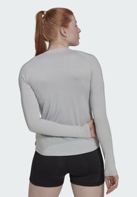 Langärmliges graues Sportoberteil mit glatter Textur und tailliertem Design, kombiniert mit schwarzen Shorts, von hinten betrachtet.