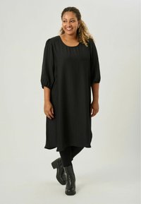 Svart klänning i texturerad tyg med lös passform, rund halsringning och puffärmar. Bärs med svarta leggins och ankelstövlar.