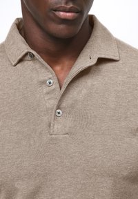 Beige Polo-Shirt mit strukturiertem Strick, mit Kragen, drei Knöpfen und einer dezenten Leiste. Klassisches Design mit minimalen Details.