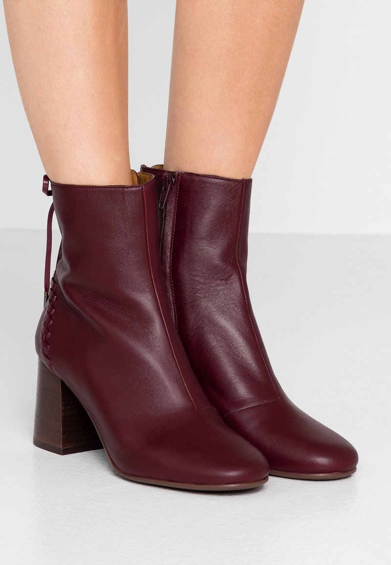 Botas de tobillo de cuero burdeos con un acabado suave, que cuentan con una cremallera lateral, tacón de bloque y costura decorativa en el lado izquierdo.