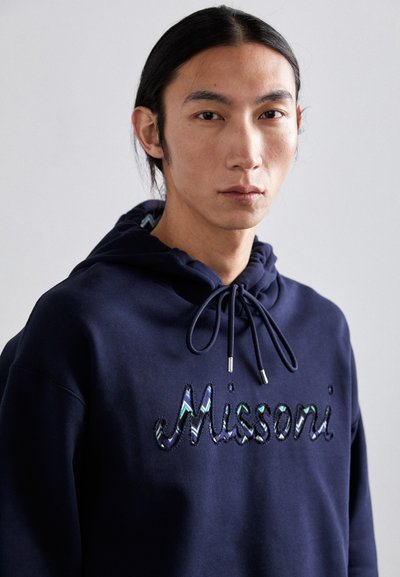 Sweatshirt azul-marinho com cordão, apresentando o texto bordado "Missoni" em cores brilhantes e variadas. Feito de um tecido suave, com um design casual.