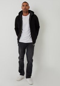 Sort ribbet zip-up hoodie med foret hætte, lagd over en hvid t-shirt, parret med mørkegrå jeans og hvide sneakers.