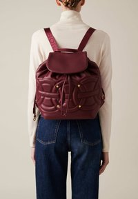 Maroon leather backpack with a rounded shape, quilted pattern, drawstring closure, and gold-tone hardware. Adjustable shoulder straps.