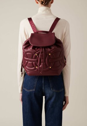 Zaino in pelle bordeaux con forma arrotondata, motivo trapuntato, chiusura a cordoncino e accessori in tono oro. Spallacci regolabili.