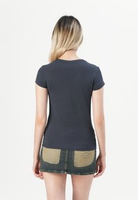 T-shirt a maniche corte, attillato, in cotone grigio scuro. Presenta un collo rotondo. Abbinato a una gonna di jeans con un pannello beige chiaro e logo.