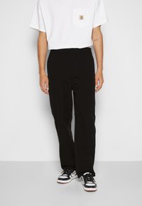 Czarne spodnie z elastycznym paskiem w talii, gładkim przodem, dwoma bocznymi kieszeniami i minimalistycznymi przeszyciami. Ubrane z białym t-shirtem i trampkami.