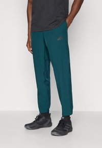 Tirkizne sportske hlače od laganog materijala, s tapered krojem i elastičnim manžetama. Adidas logo otisnut u sivoj boji na butini.