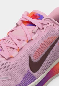 Ροζ παπούτσι τρεξίματος Nike με επάνω μέρος από πλέγμα, σκοτειλό λογότυπο swoosh, πολύχρωμες πορτοκαλί και μωβ λεπτομέρειες και δεμένα κορδόνια.