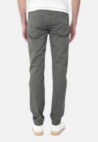 Chino slim fit da uomo in cotone grigio, con due tasche posteriori e gamba affusolata. Indossati con sneakers bianche su uno sfondo neutro.