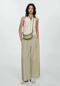 Top s nařasenou texturou, světle béžový; široké skladané kalhoty v khaki; malá olivově zelená crossbody taška; bílé slip-on sandály.